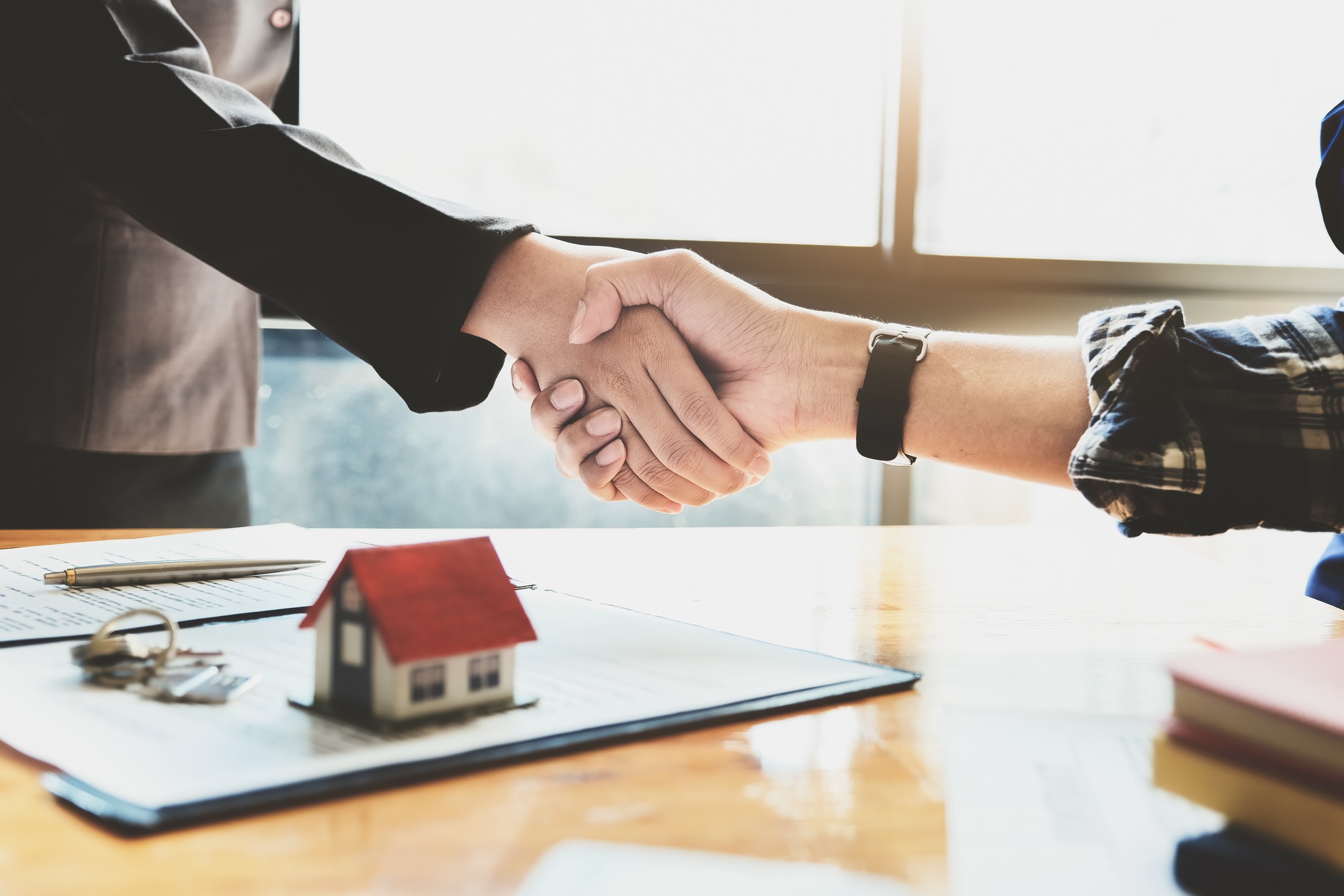 Sell Your Home For 1% San Diego with a congratulatory handshake over a table featuring a miniature house, keys, and contract papers at One Percent Realtor Fee.